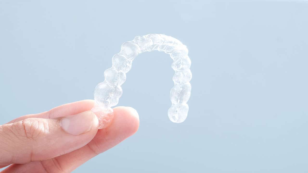 A hand holding teeth whitening tray with a blue background