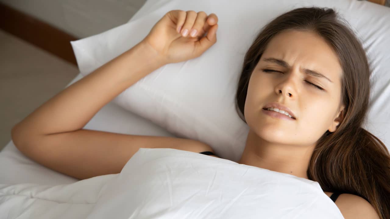 Young woman laying in bed in visible pain