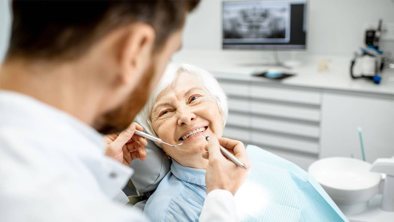 Older woman sitting in a dental chair talking to the dentist about dental implants