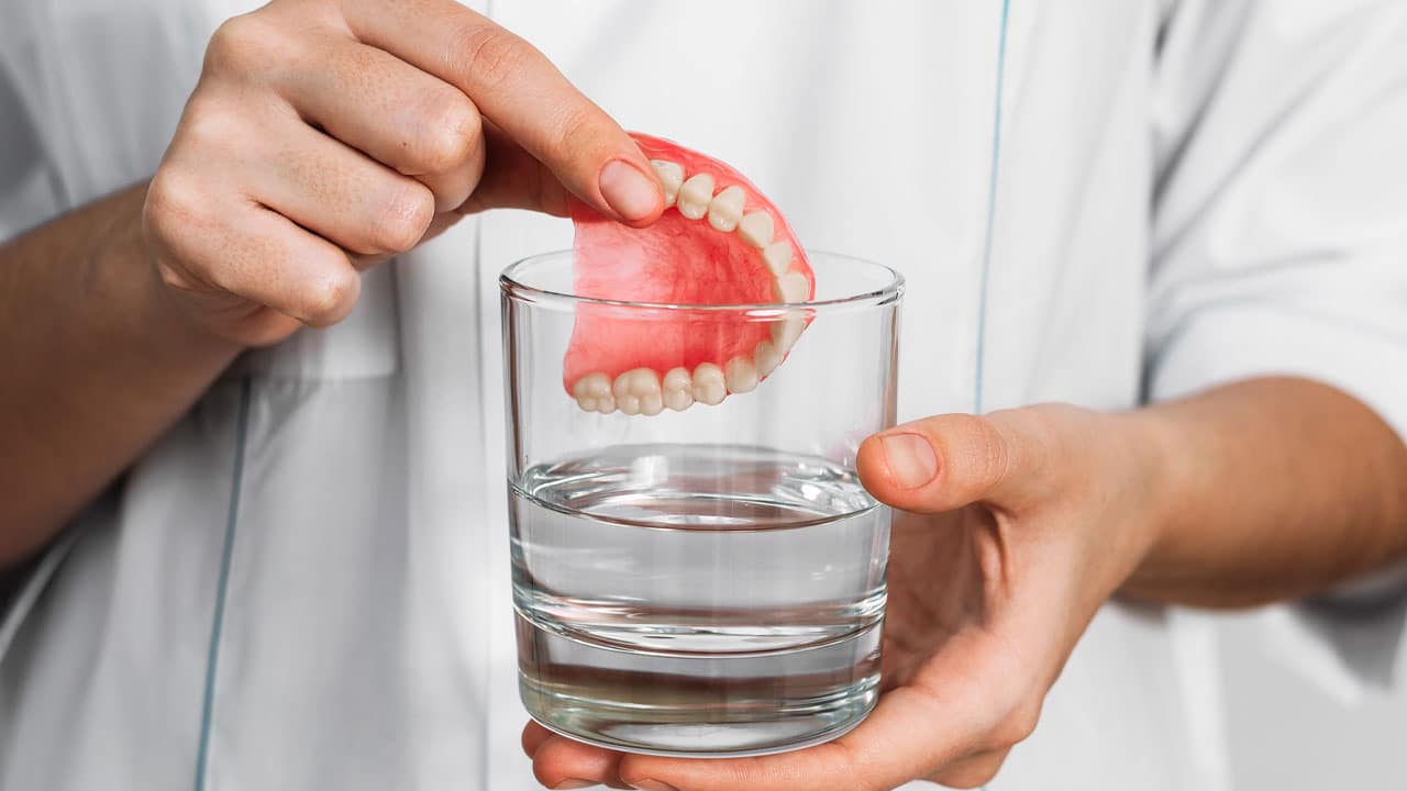 A denture being placed into a glass with a solution