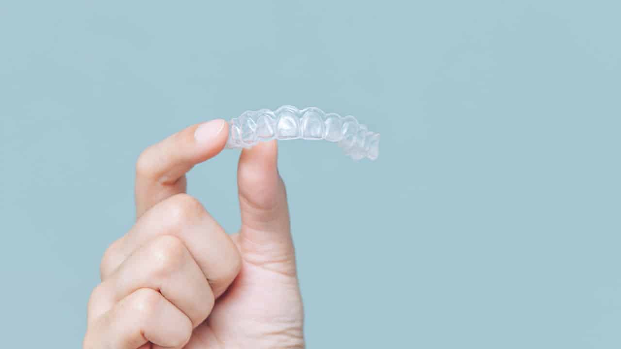 A close-up photograph of a mouthguard on a blue background. The mouthguard is designed to protect the teeth and mouth from injury during sports or other physical activities