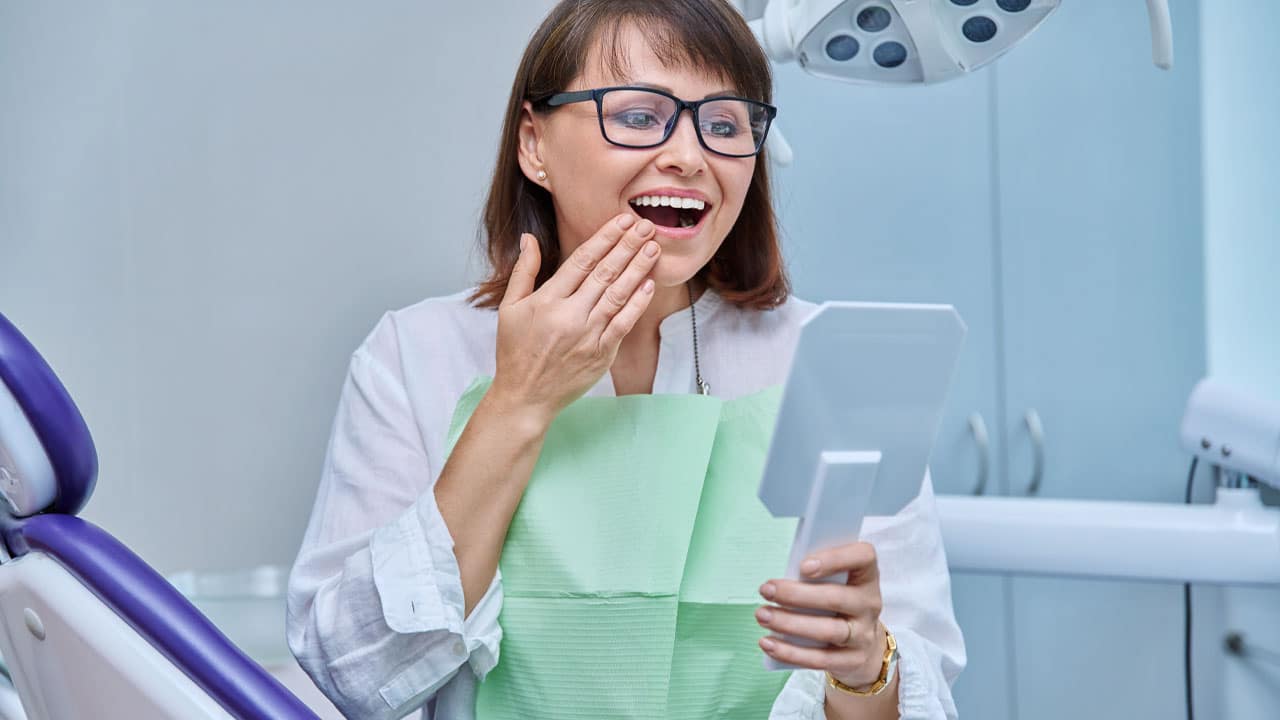 Elderly woman looking at teeth in dental mirror