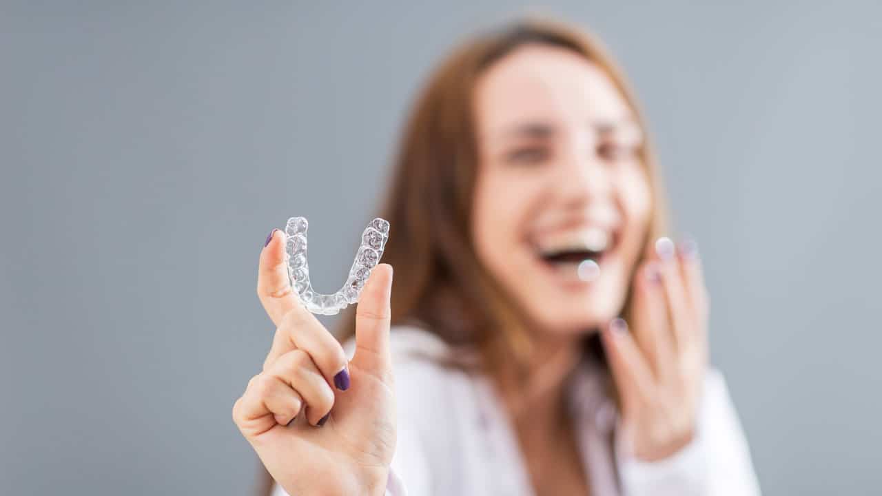 Woman holding up clear aligner tray while smiling